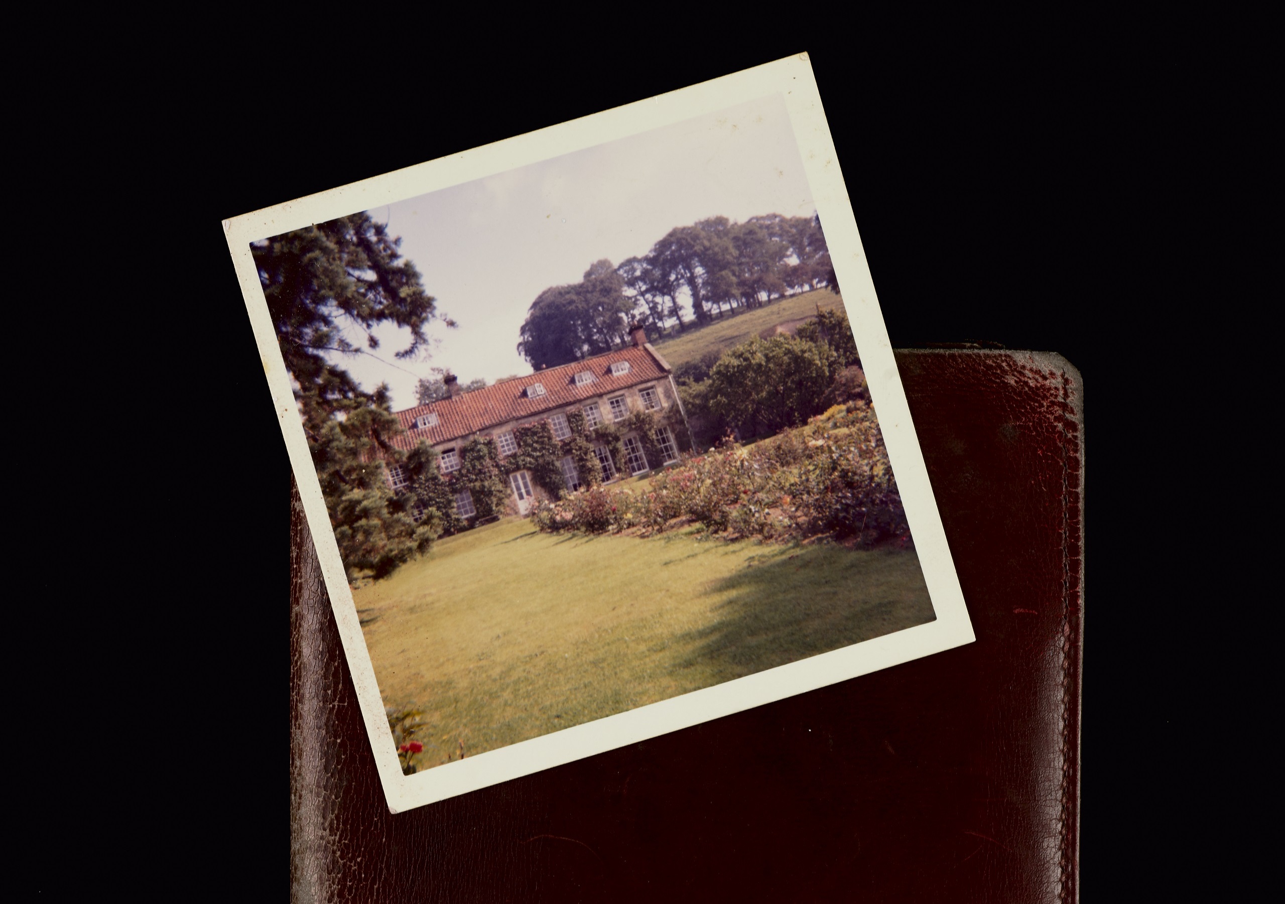 Photo of country house and garden resting on brown leather wallet